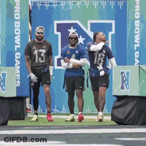 A Group Of Football Players Are Standing On A Field In Front Of A Sign That Says Pro Bowl Games GIF