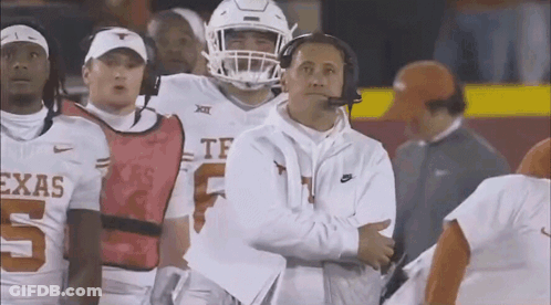 A Group Of Football Players Are Standing On A Field With A Coach Standing Behind Them . GIF