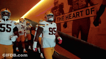 A Group Of Football Players Are Walking Down A Hallway With A Sign That Says The Heart Of GIF