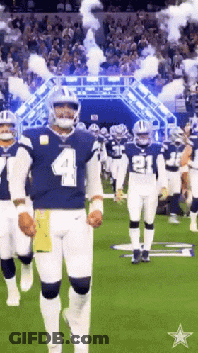 A Group Of Football Players Are Walking On A Field With Smoke Coming Out Of The Tunnel . GIF
