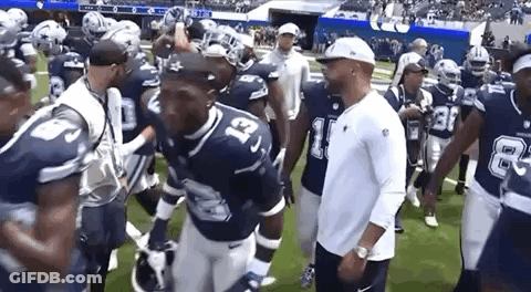 A Group Of Football Players Are Walking On A Field With Their Coach . GIF