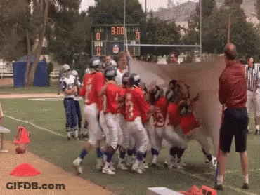 A Group Of Football Players On A Field With A Scoreboard In The Background GIF