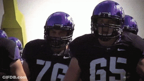 A Group Of Football Players Wearing Purple Helmets And Jerseys With The Number 76 And 65 On Them GIF