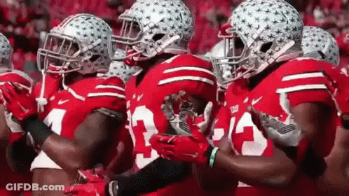 A Group Of Football Players Wearing Red Jerseys And Helmets Are Standing In A Line . GIF
