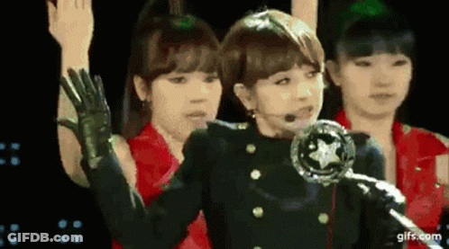 A Group Of Girls Are Standing On A Stage With Their Arms In The Air . GIF