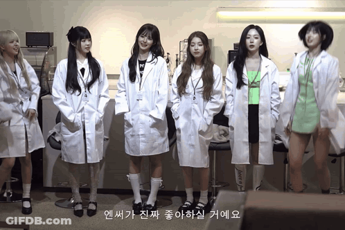A Group Of Girls In Lab Coats Are Standing In A Line GIF