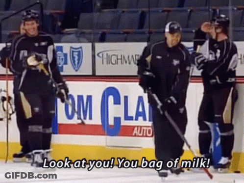 A Group Of Hockey Players Are Standing On A Rink With A Sign That Says Look At You You Bag Of Milk GIF