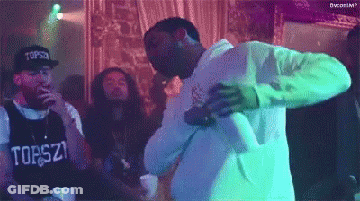 A Group Of Men Are Dancing In A Room With A Man Wearing A Shirt That Says ' Tops ' On It . GIF