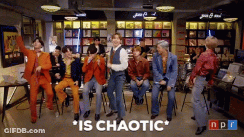A Group Of Men Are Dancing In A Room With The Words " Is Chaotic " Above Them GIF