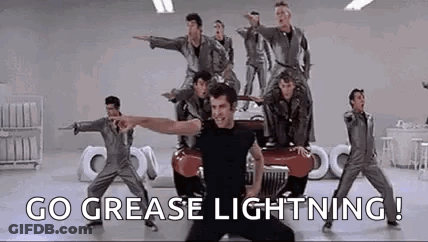 A Group Of Men Are Dancing In Front Of A Car With The Words `` Go Grease Lightning ! '' GIF