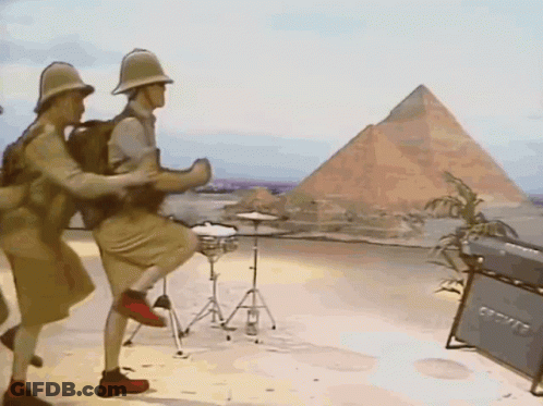 A Group Of Men Are Dancing In Front Of A Pyramid In The Desert GIF