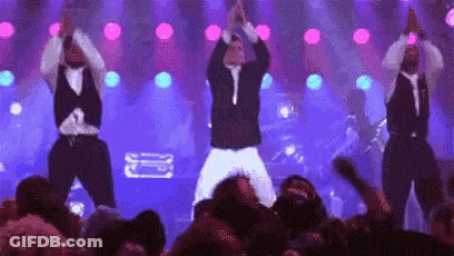 A Group Of Men Are Dancing On Stage In Front Of A Crowd . GIF