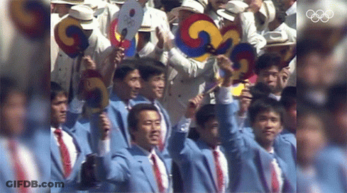A Group Of Men Are Holding Up Their Fans In Front Of The Olympics Logo GIF