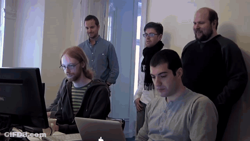 A Group Of Men Are Looking At A Laptop With An Apple Logo GIF
