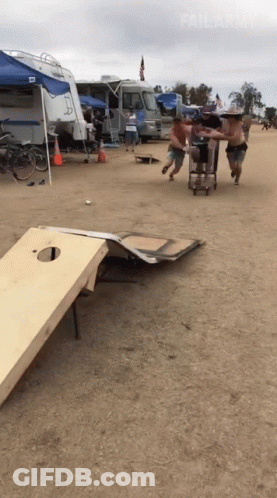 A Group Of Men Are Playing A Game Of Cornhole On A Sandy Field GIF