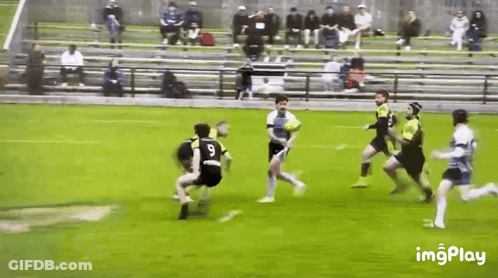 A Group Of Men Are Playing A Game Of Rugby On A Field With Bleachers In The Background . GIF