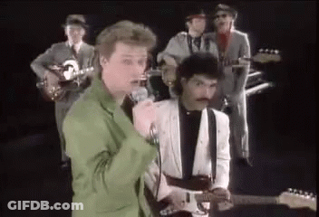 A Group Of Men Are Playing Guitars And Singing Into Microphones While Standing Next To Each Other On A Stage . GIF