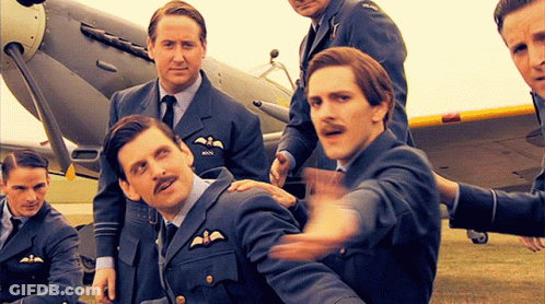A Group Of Men Are Posing For A Picture In Front Of An Airplane And One Of Them Has The Letters Rnn On His Chest GIF