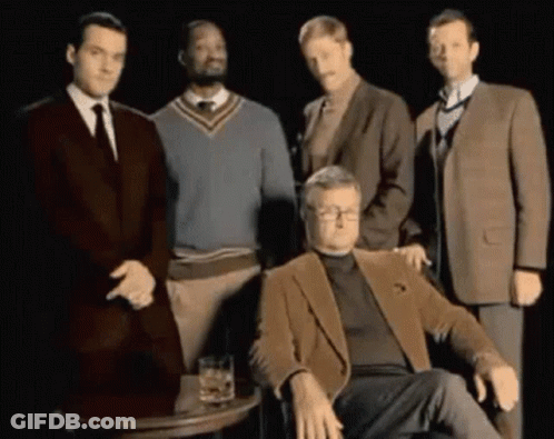 A Group Of Men Are Posing For A Picture With One Man Sitting In Front Of A Table With A Glass Of Whiskey GIF