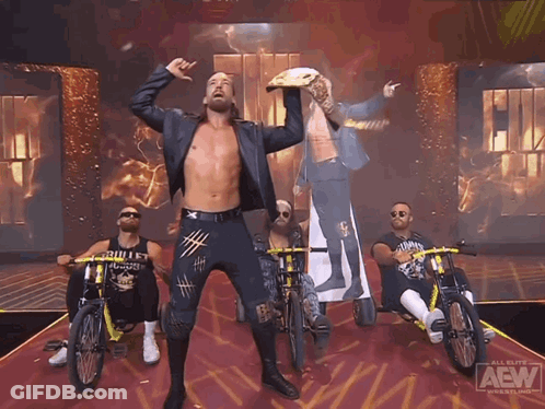 A Group Of Men Are Riding Bikes On A Stage That Says Aew On It GIF