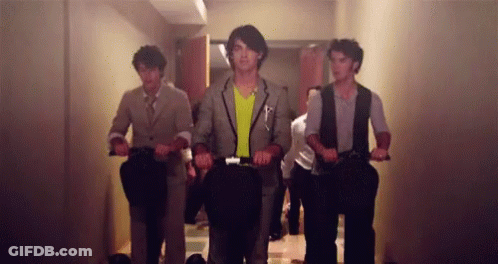 A Group Of Men Are Riding Scooters In A Hallway GIF