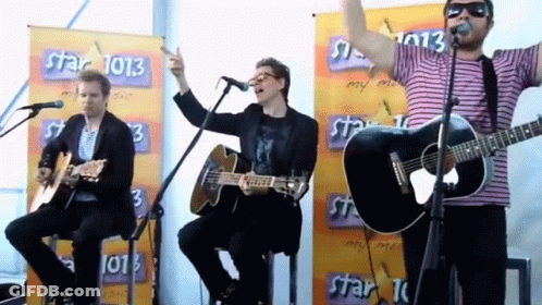A Group Of Men Are Singing And Playing Guitars In Front Of A Banner That Says Star 1013 GIF