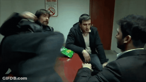 A Group Of Men Are Sitting Around A Table With A No Smoking Sign Behind Them GIF