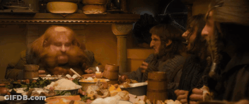 A Group Of Men Are Sitting Around A Table With Food And Drinks GIF