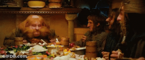 A Group Of Men Are Sitting Around A Table With Plates Of Food . GIF