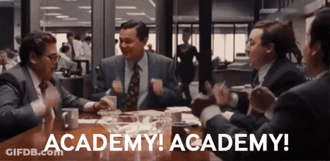 A Group Of Men Are Sitting Around A Table With The Words Academy Academy Written On The Table GIF