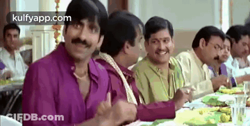 A Group Of Men Are Sitting At A Long Table Eating Food . GIF