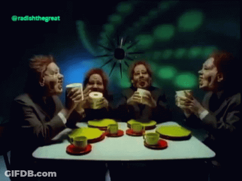 A Group Of Men Are Sitting At A Table Drinking Tea And Eating Donuts GIF