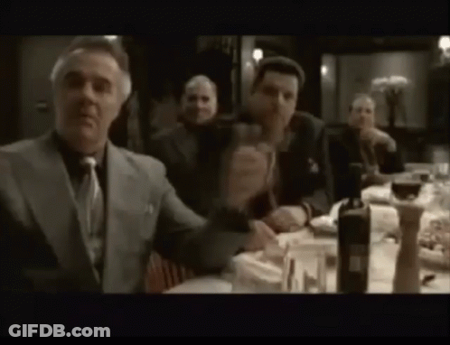 A Group Of Men Are Sitting At A Table Drinking Wine And Eating Food . GIF