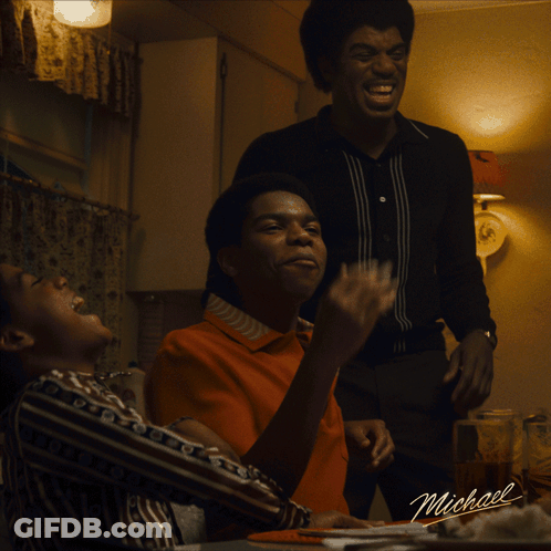 A Group Of Men Are Sitting At A Table With A Sign That Says Michael On It GIF