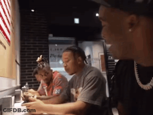 A Group Of Men Are Sitting At A Table With One Wearing A T-Shirt That Says Do GIF
