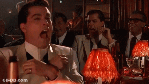 A Group Of Men Are Sitting At A Table With Red Lamps And Laughing GIF