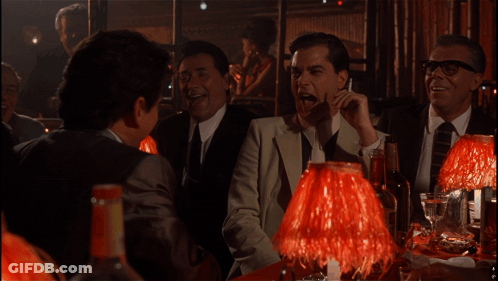 A Group Of Men Are Sitting At A Table With Red Lamps In A Dark Room GIF