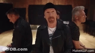 A Group Of Men Are Sitting In A Room And One Of Them Has A Beard And A Black Jacket On . GIF