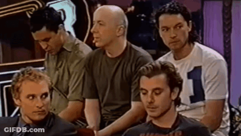 A Group Of Men Are Sitting In A Row And One Of Them Is Wearing A Shirt With The Number 1 On It . GIF