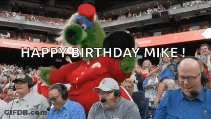 A Group Of Men Are Sitting In A Stadium With A Mascot And The Words `` Happy Birthday Mike '' . GIF