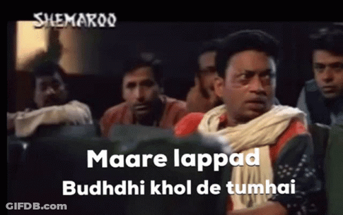 A Group Of Men Are Sitting In A Theater Watching A Movie And One Of Them Is Wearing A White Scarf Around His Neck . GIF