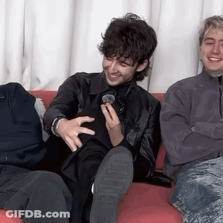A Group Of Men Are Sitting On A Couch Laughing And Holding A Microphone . GIF