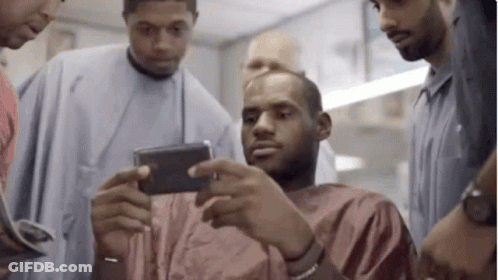 A Group Of Men Are Standing Around A Man In A Barber Shop . GIF