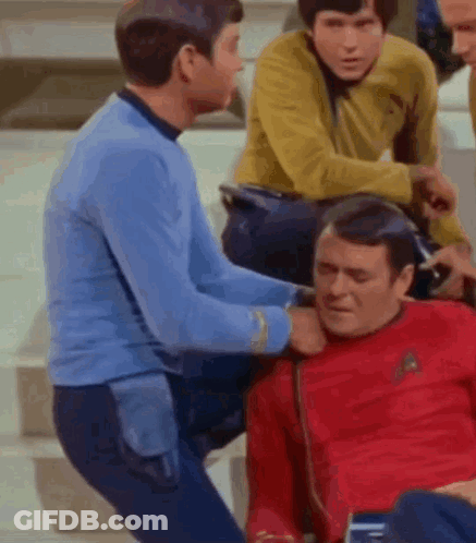 A Group Of Men Are Standing Around A Man In A Red Shirt Who Is Laying On The Ground . GIF