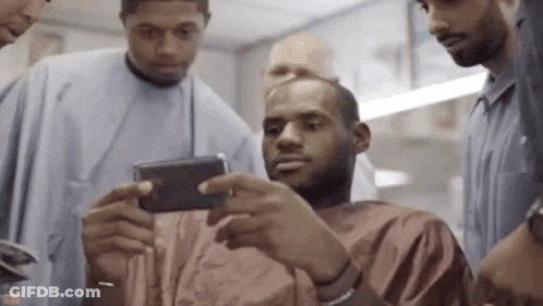 A Group Of Men Are Standing Around A Man Taking A Picture Of Himself With His Phone . GIF