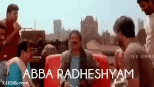 A Group Of Men Are Standing Around A Red Couch And Talking To Each Other . GIF