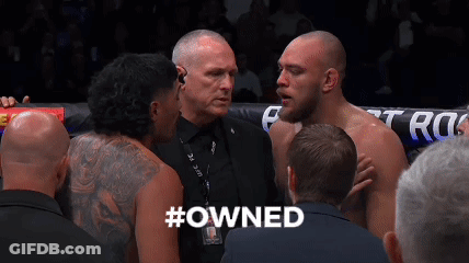 A Group Of Men Are Standing In A Boxing Ring And One Of Them Has The Word #Owned On His Back GIF