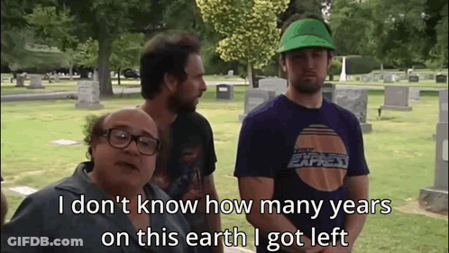 A Group Of Men Are Standing In A Cemetery And One Of Them Is Wearing A Green Hat GIF