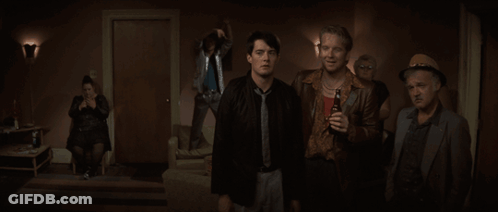 A Group Of Men Are Standing In A Dark Room And One Of Them Is Holding A Bottle Of Beer GIF