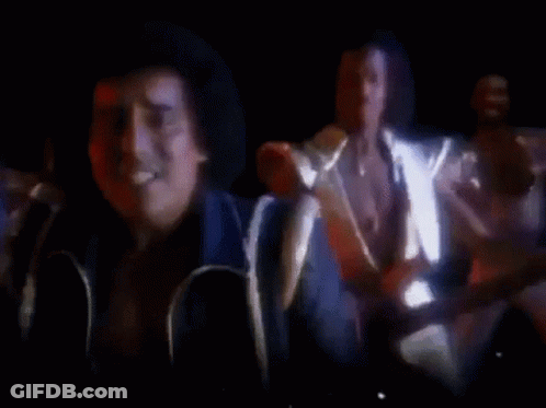 A Group Of Men Are Standing In A Dark Room Playing Guitars And Singing . GIF